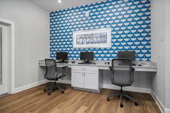 Two computers on a desk in front of a blue patterned wall.